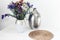 Bouquet of flowers, metal vase and straw wicker stand on the table, cozy home interior