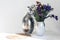 Bouquet of flowers, metal vase and straw wicker stand on the table, cozy home interior