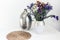 Bouquet of flowers, metal vase and straw wicker stand on the table, cozy home interior