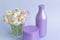 A bouquet of fresh flowers, daisies on green stems are in a glass with clean water and two purple jars with cream cosmetics on a