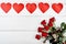 Bouquet of fresh red roses and garland of paper hearts on wood table, copy space. Greeting card mockup for Valentines day. Love