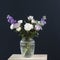Bouquet of hackelia velutina, purple and white roses, small tea roses, matthiola incana, blue iris in glass vase opposite on black