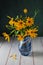 A bouquet of Jerusalem artichoke flowers in a blue glass jug on a white wooden background. Autumn flowers, compositions, decor