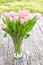Bouquet of light pink tulips on the oak brown table in a clear g