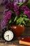 Bouquet of lilac flowers in a ceramic pot with a black alarm clock