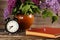 Bouquet of lilac flowers in a ceramic pot with a black alarm clock