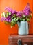 Bouquet of lilac in an old enameled teapot on vintage suitcase on yellow background. Retro style still life.