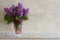 Bouquet of lilacs in glass vase on background wall of travertine. Flavor of spring flowers