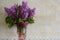 Bouquet of lilacs in glass vase on background wall of travertine. Flavor of spring flowers