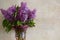 Bouquet of lilacs in glass vase on background wall of travertine. Flavor of spring flowers