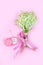 A bouquet of lily of the valley flowers with pink ribbons and a pink box with a gold bracelet on a pink background