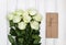Bouquet of luxurious white roses and a present box in eco paper on white wooden background. Top view, flat lay