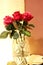 A bouquet of red roses in a crystal vase in the evening on a table, brown and beige tones