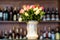 Bouquet of roses in a white ceramic vase counter against the shelf of bottles.