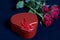 A bouquet of scarlet roses and a gift in a box in the shape of a heart.