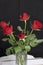 A bouquet of scarlet roses in a glass vase. Five flowers. On a black background