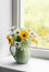 A bouquet of summer flowers of daisies, hydrangeas in a vintage ceramic jug on the window in a bright room