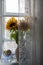 A bouquet of sunflowers in a clay jug and a bowl with cookies on the windowsill behind a lace curtain