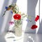 Bouquet of three red poppy flowers and different wildflowers in crystal vase with water on white table with contrast sun light and