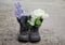 Bouquet of white and lilac flowers in dirty soldier`s boots in the spring garden