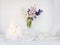 A bouquet of white, pink, blue cut hyacinth in a small white corrugated vase and three large burning candles on a round tray are