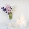 A bouquet of white, pink, blue cut hyacinth in a small white corrugated vase and three large burning candles on a round tray are