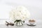 A bouquet of white roses in a round glass vase on a table with a cup of tea and a wrapped rolled paper