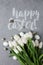 A bouquet of white tulips and chicken and quail eggs with lettering sign Happy Easter on a gray concrete background. Top