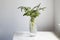 A bouquet of white veronica with white bells in a tall narrow vase on a grey table on the