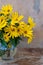 A bouquet of yellow Jerusalem artichoke flowers in a glass vase on a wooden background. Postcard with place for text. A simple