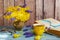 Bouquet of yellow primroses and muscari in a vase. Wooden background, book, yellow cup, glasses.