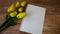 A bouquet of yellow tulips next to a blank sheet of paper