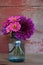 A bouquet of zinnias and dahlias in a blue canning jar with a re