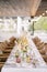 Bouquets of flowers stand on a long festive table with wicker chairs around