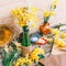 Bouquets of yellow daffodils flowers in a vase and a pitcher of Kraft paper and colored ribbons with a Hank of rope on a wooden ta