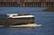 Bow of inland vessel at full speed with white foaming bow wave and pier in the background