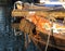 Bow of an old rusty iron canal boat moored with ropes on a jetty with reflections in dark water