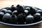 Bowl of black olives. Black canned pitted olives in a dark blue glass bowl on a rustic wooden table.