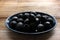 Bowl of black olives. Black canned pitted olives in a dark blue glass bowl on a rustic wooden table.
