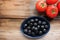 Bowl of black olives and fresh tomatoes on the vine on rustic wooden table background. Pasta or salad ingredients.