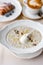 Bowl of breakfast oatmeal with soft Italian cheese and cinnamon. Croissants, coffee and other dishes on the table in the