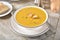 A bowl of butternut squash soup with a dinner roll