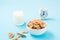 A bowl of cereal, a glass of milk and an alarm clock on a blue background. Scheduled breakfast