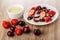 Bowl with condensed milk, cherries and strawberries with condensed milk in saucer, berries on table