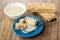 Bowl with condensed milk, milk poured on broken puffed rice, spoon in saucer, puffed rice on table