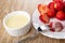 Bowl with condensed milk, strawberries in plate, berry strung on fork on wooden table