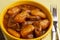 Bowl with cooked cassava and meat on wooden table