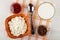 Bowl with cottage cheese, spoon, bowl with sour cream, small bowls with jam and raisin on napkin on wooden table. Top view