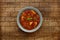 A bowl of delicious minestrone soup, topped with a sprig of basil, in a rustic bowl, on a checked wooden background