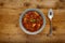 A bowl of delicious minestrone soup, topped with a sprig of basil, in a rustic bowl, on a wooden background, with a silver spoon